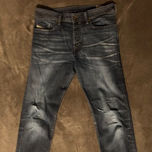 Mörkblå jeans med slitningar från diesel - Snygga mörkblå jeans med slitningar på knäna för en trendig look. De har en klassisk femficksdesign och knappgylf. Perfekta för en avslappnad stil. Storlek W31 L34