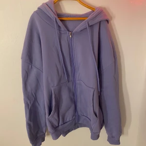 Ljuslila hoodie med dragkedja - Säljer en mysig ljuslila hoodie med dragkedja och huva. Perfekt för en avslappnad stil. Den har långa ärmar och praktiska fickor framtill.