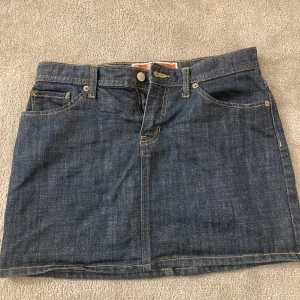 Jeanskjol från GAP - Snygg jeanskjol från GAP med klassisk femficksdesign och knappstängning fram. Perfekt för en avslappnad stil. Kjolen har en kort längd och är tillverkad i slitstarkt denimtyg.