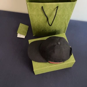 Svart keps från Gucci - Snygg svart keps från Gucci med diskret mönster och klassisk design. Kepsen har en justerbar rem baktill för perfekt passform. Perfekt för att ge en lyxig touch till din outfit.