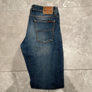  Nudie Jeans Tube Kelly - Snygga mörkblå jeans från Nudie Jeans med klassisk femficksdesign och orange sömmar. De har en knappgylf och en läderpatch med logotyp baktill. Perfekta för en stilren look. Pris kan såklart diskuteras!