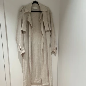 Trenchcoat liknande  - Snygg beige Linné trenchcoat från Nelly i ett lätt och luftigt material. Jackan har långa ärmar och en klassisk krage. 