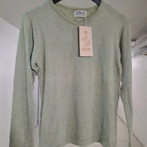 Grön långärmad tröja från Cica - Snygg och enkel grön långärmad tröja från Cica. Perfekt för en avslappnad stil. Tröjan har en rund halsringning och är tillverkad i ett mjukt material som känns skönt mot huden. Helt  ny oanvänd 
