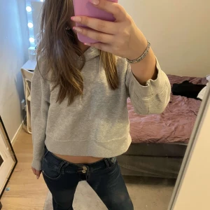Grå croppad hoodie - Säljer en stilren grå croppad hoodie med långa ärmar. Perfekt för en avslappnad look. Den är mjuk och bekväm, idealisk för vardagsbruk.