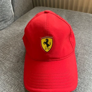 Ferrari keps-Officiell produkt - Officiell Ferrari keps i röd färg. Tillverkad av 97% polyester och 3% elastan. Insidan är 100% polyester. Kepsens baksida har ventilationshål. Perfekt för Formel 1-fans eller Ferrari-entusiaster. Använd 1-2 gånger. Nypris runt 400 kr. 🚫Djurfritt och rökfritt hem 