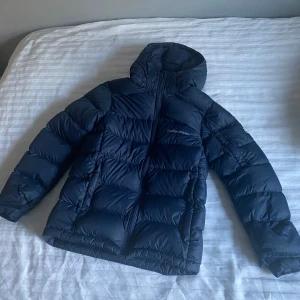 Marinblå Peak Performance JR Frost Down Jacket stlk 150 - Säljer en marinblå dunjacka från Peak Performance. Perfekt för kalla dagar när du vill hålla dig varm och bekväm. OBS! Juniorstorlek 150