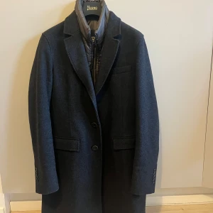 Herno jacka - Elegant mörkblå kappa från Herno med klassisk design. Kappan har långa ärmar och knappar framtill. Den är tillverkad i ett stilrent material och har en quiltad insida för extra värme. Perfekt för kyligare dagar. Är i nyskick och använda ental gånger. Fråga om du undrar något. Pris ej hugget i sten. Innefodret går att plocka av.