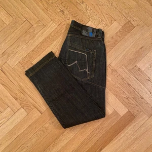 Mörkblå Blend Jeans - Snygga mörkblå jeans från Blend med cool wash och unikt broderi på bakfickorna samt knappgylf. Säljer för att de inte passade mig. Är i nyskick utan prislapp, inga tecken på användning. Perfekta för en avslappnad stil. W32 Kan ge mer exakta mått vid frörfrågan. 