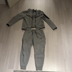 Grå och olivgrön träningsset från Nike - Säljer ett stilrent träningsset från Nike i grått,vitt,vitt/gul, röd/blå,svart/grå och olivgrönt. Setet består av en långärmad tröja med dragkedja och matchande byxor med snörning i midjan. Perfekt för träning eller en avslappnad dag. Finns även i fler färgkombinationer men dom som finns i sätt det ni på bilderna. STORLEK S,M,L