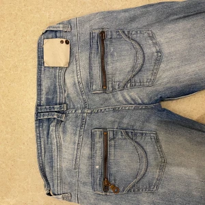 Blåa låg midjade jeans  - Snygga blå jeans från Sticko 19 med slitningar på benen och dubbla knappar i midjan. De har en klassiska fickor med dragkedja bak på fickorna. Perfekta för en cool stil. Skriv vid mått och längd eller vid andra frågor och funderingar! Säljer för att dem är för stora för mig 🩷