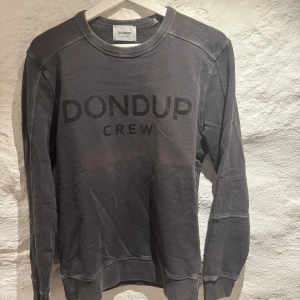 Grå sweatshirt från Dondup - Snygg grå sweatshirt från Dondup med texten 'DONDUP CREW' tryckt på framsidan. Tröjan har långa ärmar och ribbade muddar vid ärmslut och nederkant. Perfekt för en avslappnad stil.. Den är i väldigt bra skick och den har bara anvädts varsamt, pris kan diskuteras och var nu inte rädd att höra av dig vid några funderingar😉🤩