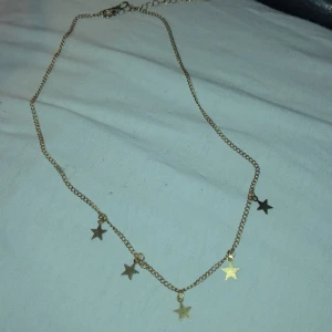 Guldhalsband med stjärnor - Snyggt guldhalsband med små stjärnberlocker som hänger längs kedjan. Perfekt för att lägga till en touch av stjärnglans till din outfit. Kedjan är tunn och elegant, vilket gör den lätt att bära till olika tillfällen.