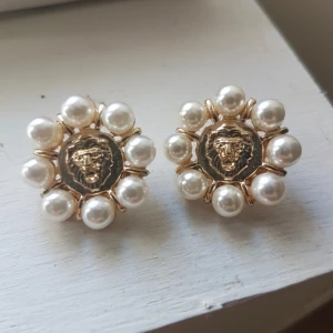Guldörhängen med pärlor och lejonmotiv - Eleganta guldörhängen med ett centralt lejonmotiv omringat av vita pärlor. Perfekta för att ge en lyxig touch till din stil.
