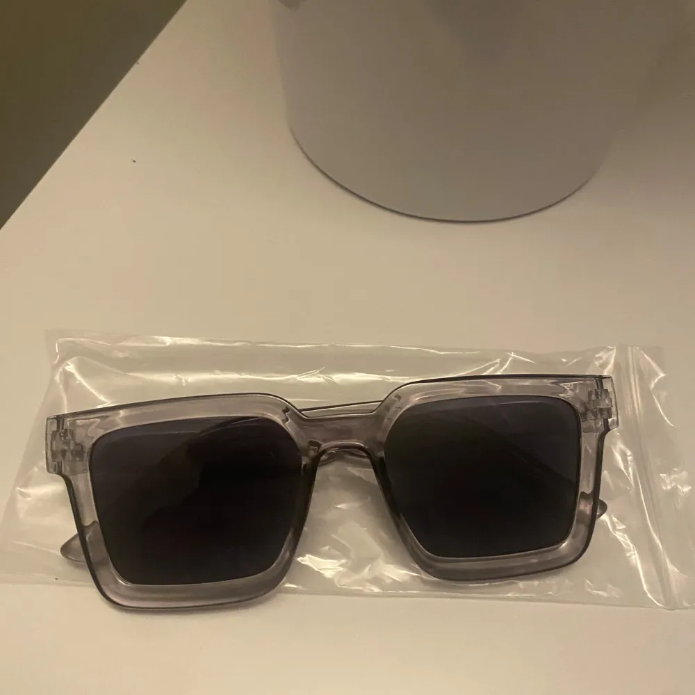 Snygga solglasögon med transparent båge och fyrkantig form. Perfekta för en stilren look. De mörka glasen ger ett coolt intryck och skyddar mot solen. Passar både till vardag och speciella tillfällen. Asusteet.