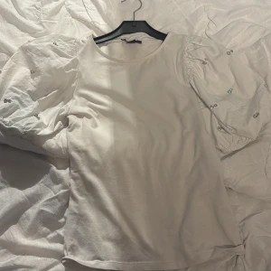 Vit topp från Amisu - Säljer en söt vit topp från Amisu med puffiga kortärmar och små broderade detaljer. Perfekt för en stilren look. 