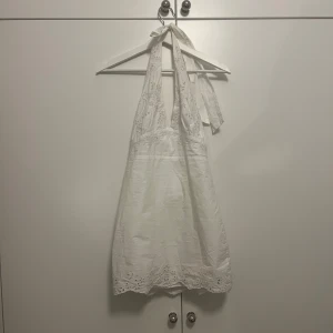 Vit halterneck klänning med spetsdetaljer - Säljer en söt vit klänning med spetsdetaljer och knytband i nacken (halterneck). Klänningen har fina broderade blommor längs halsringningen. Storlek xs från zara, går att använda som topp också! Använd 1 gång, inga defekter💞 perfekt till studenten eller sommaren !! 