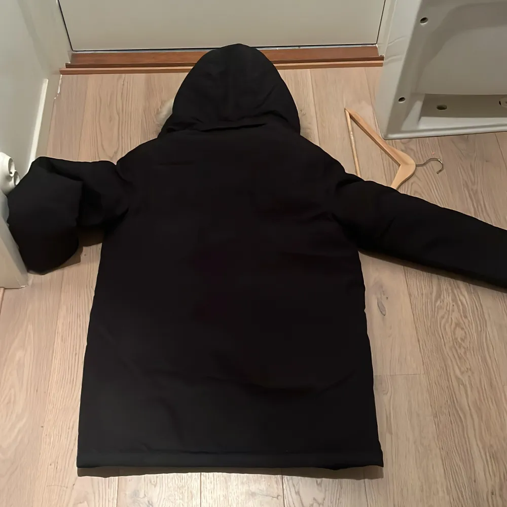 Säljer en stilren svart parkajacka från Tommy Hilfiger med pälskantad huva. Jackan har långa ärmar och praktiska fickor med knappar framtill. Perfekt för kyliga dagar.. Takit.