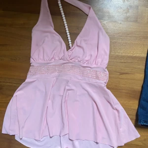 Rosa halterneck topp från X Collection - Säljer en söt rosa halterneck topp från X Collection. Toppen har en djup v-ringning och ett brett band under bysten med fina detaljer. Perfekt för sommarens fester eller en dag på stan!