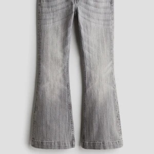 Grå flared jeans från H&M - Säljer ett par snygga grå flared jeans från H&M. De har en cool vintage-look med en lätt tvättad effekt. Byxorna har en hög midja och en utsvängd bootcut-stil som ger en retro vibe. Bakfickorna är dekorerade med en söt rosett-detalj och knappar. Perfekta för både vardag och fest!