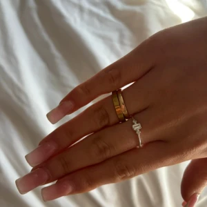 Guldring med gravyr - Säljer en stilren guldring med en elegant gravyr. Ringen har en slät yta och är perfekt för både vardag och fest. Den är i nyskick och ger en lyxig känsla till vilken outfit som helst. Rostfri