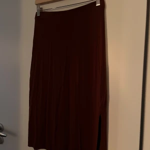 Brun kjol från Lindex - Säljer en snygg brun kjol från Lindex i storlek S. Kjolen har en stilren design med en slits på sidan som ger den lite extra edge. Perfekt för både vardag och fest! Materialet känns mjukt och bekvämt.