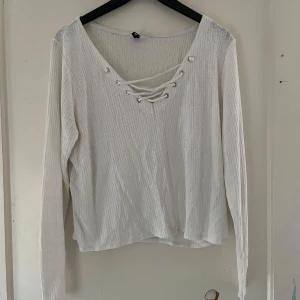 Vit ribbad tröja från Divided - Säljer en snygg vit ribbad tröja från Divided. Den har långa ärmar och en cool snörning framtill som ger en extra detalj. Perfekt för både vardag och fest! 🖤