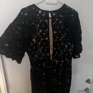 Svart spetsklänning från H&M - Säljer en elegant svart spetsklänning från H&M. Öppen och fin rygg. Klänningen har ett vackert blommigt mönster och korta ärmar. Perfekt för festliga tillfällen! Den har en normal passform och är i nyskick. Passar perfekt till middag och fester.