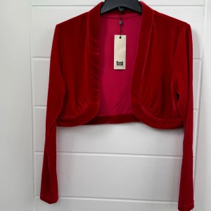 eleganta röda sammetkofta, Helt Ny. - Denna sammetkofta från Flash Woman är helt ny med prislapp.   Mätningarna för denna kofta är 35 cm i längd och 48 cm i beredd, vilket gör den bekväm och passande för olika kroppstyper.   Ordinarie priset för denna sammetkofta är 299,  nu endast 149kr