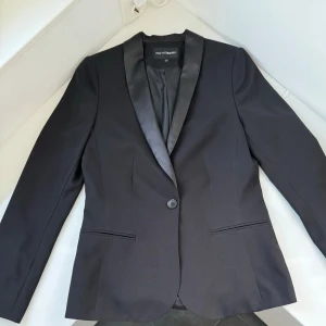 Elegans Kavaj, Helt Ny. - Denna eleganta svarta kavaj från Kappahl.Den är helt ny och utan prislapp. Kavajen har en längd på 64 cm,  beredd 44 Cm Materialet är av hög kvalitet, vilket ger kavajen en lyxig känsla och hållbarhet.  Ordinarie priset var 899kr, men nu endast 129kr