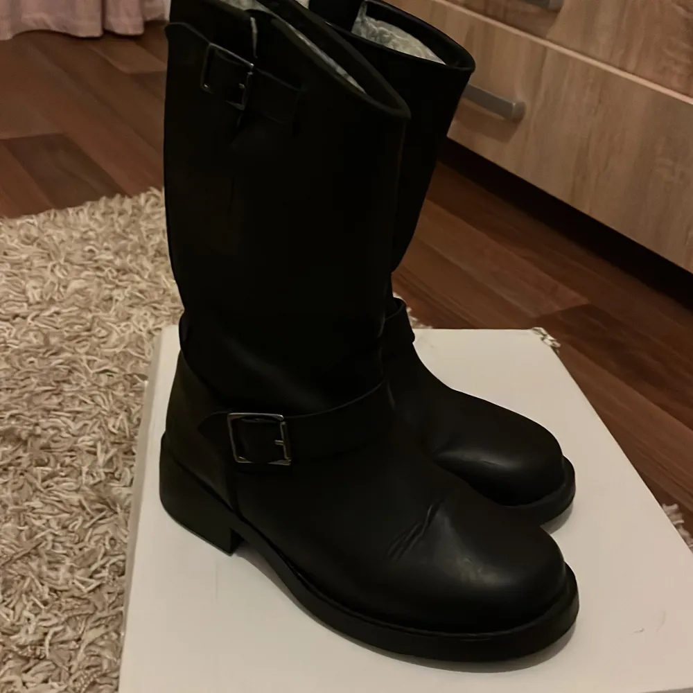 Säljer ett par svarta boots från Ella of Sweden i storlek 39. De är gjorda i skinn och har en snygg spänndetalj på sidan. Insidan är fodrad med mjukt material för extra värme och komfort.  Använt bara ett par gånger. Perfekta för höst och vinter! . Skor.