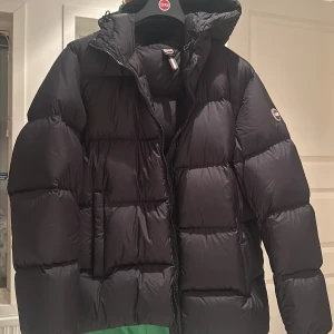 Svart pufferjacka från Colmar - Säljer en svart pufferjacka från Colmar med dragkedja och huva. Jackan är perfekt för kalla dagar och har en stilren design med långa ärmar. Den är quiltad för extra värme och komfort.Helt ny med prislapp på.