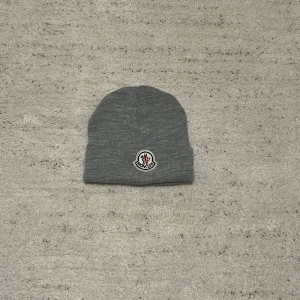Moncler mössa - Snygg grå mössa från Moncler med broderad logotyp framtill. Perfekt för kyliga dagar och en stilren look.