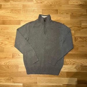 Grå quarter zip tröja från Tommy Hilfiger - Säljer en snygg grå quarter zip tröja från Tommy Hilfiger i bomull med ribbade detaljer. Perfekt för en avslappnad och snygg look.