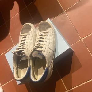 Vita sneakers från Philippe Model - Snygga vita sneakers från Philippe Model med blå detaljer. Skorna har en klassisk design med snörning och är perfekta för en stilren look. De kommer i originalkartong. Och de har en liten slitning på sulan priset är inte hugget i sten