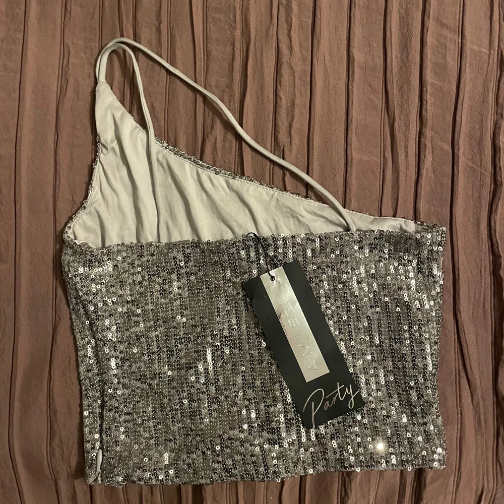 Snygg silverfärgad oneshoulder topp från Amisu, täckt med glittrande paljetter. Helt ny med prislapp💗. Yläosat.
