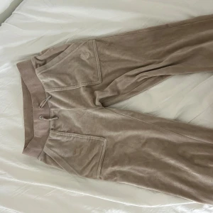 Beige mjukisbyxor från Juicy Couture - Säljer ett par snygga beige mjukisbyxor från Juicy Couture. Byxorna har en broderad logga och snörning i midjan för en perfekt passform. Perfekta för en avslappnad stil. Pris kan diskuteras. Sitter på mig som har S så dom är väldigt stretchiga 