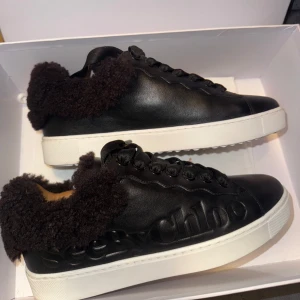 Svarta sneakers från See by Chloé - Svarta sneakers i skinn från See by Chloé med fluffig pälsdetalj runt kanten. Skorna har en vit sula och snörning framtill. Endast använda en gång.