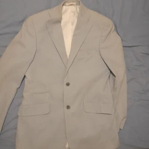 Unik kavaj från Bostin - Snygg grå kavaj från Bostin med två knappar framtill och klassiska fickor. Perfekt för en stilren look. Fodrad med ett mönstrat tyg för extra komfort. Storlek 48 helt ny aldrig använd.