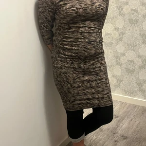 Mönstrad klänning med trekvartsärm - Snygg mönstrad klänning i mörka toner med trekvartsärm. Perfekt för en stilren look. Klänningen har en figurnära passform och är tillverkad i ett mjukt material.
