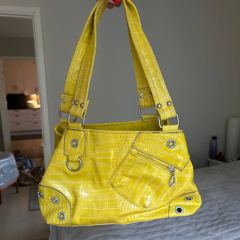 Snygg gul axelväska med krokodilmönster. Leopardmönster på innerfodret. Neongul. Väskan har flera fack med dragkedja och en unik design med nitar och ringdetaljer. Perfekt för att lysa upp din outfit! . Laukut & Käsilaukut.