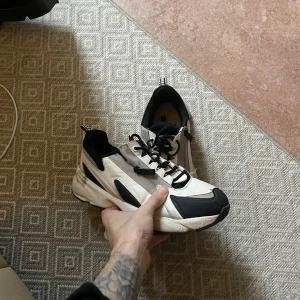 Vit svarta sneakers - Vita skor med svarta detaljer och dragkedja.    Snygga skor med dragkedja och snören. Skorna saknar sula och har spruckna hälar på insidan där av de billiga priset.   Välkommen att testa på plats alternativt fraktar med postnord/schenker