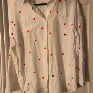 Vit skjorta med röda hjärtan från Shein - Säljer en söt vit skjorta från Shein med röda hjärtan över hela tyget. Skjortan har långa ärmar och knappar framtill. Skjortan är stor (oversize)