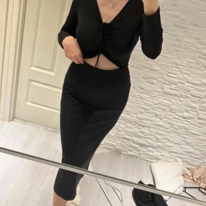 Svart långklänning med knyt - Elegant svart långklänning med v-ringning och knyt framtill. Klänningen har långa ärmar och en stilren design med en liten öppning vid midjan. Passar perfekt för s/m/l storlek