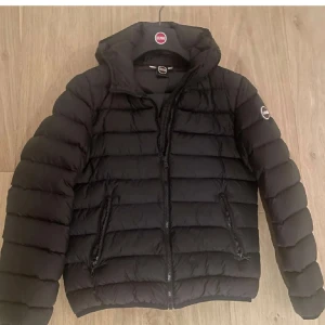  Colmar Jacka - Säljer en stilren svart pufferjacka från Colmar. Jackan har en quiltad design med dragkedja framtill och två praktiska fickor med dragkedjor. Perfekt för kyligare dagar med sin varma och bekväma passform.