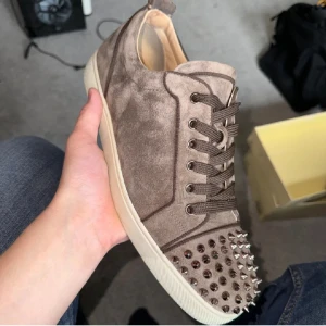 Louboutin skor - BRA PRIS!! Snygga beiga sneakers i mocka från Louboutin med coola nitar på tån. Självklart äkta, Skorna har snörning och en bekväm sula. Perfekta för att ge din outfit en edgy touch. En nitar missar men inget man märker av, kan mötas i Stockholm och skicka, billigt pris för måste få dom sålda