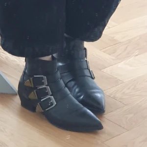 Svarta boots med spännen från &Other Stories - Snygga svarta boots i skinn med spetsig tå och tre dekorativa spännen på sidan. 