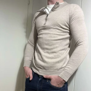 Beige merinoull halfzip - Snygg beige långärmad tröja med dragkedja vid halsen. Perfekt för en stilren och avslappnad look. Passar bra till jeans.