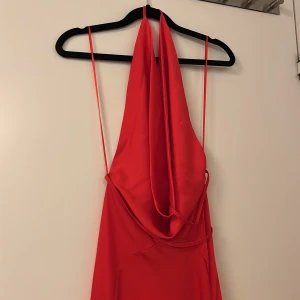 Röd långklänning med öppen rygg - Elegant röd långklänning med tunna axelband och en vacker öppen rygg. Klänningen har en flytande design som ger en smickrande silhuett. Perfekt för speciella tillfällen.