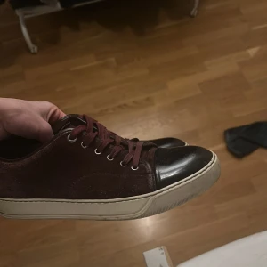 Lanvin vinröda - Snygga vinröda sneakers från Lanvin med vit sula. Skorna har snörning och en stilren design som passar perfekt för en avslappnad look. Passar 42-43.
