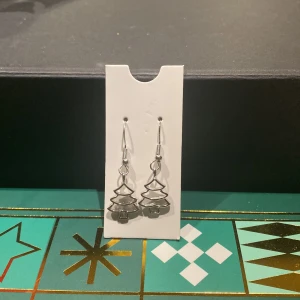 Silverfärgade julgransörhängen - Charmiga örhängen i form av julgranar i silverfärg. Perfekta för att addera en festlig touch till din look under julen. Lätta att bära med krokfäste.